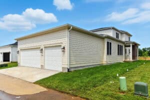 A new residential house with attached garage, siding, and green lawn in a suburban neighborhood.