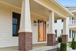 Front porch of a modern house with brick columns and a wooden front door.
