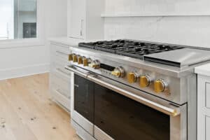Stainless steel gas stove in a modern kitchen with white cabinets and marble backsplash.