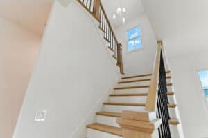 Interior view of a staircase featuring wooden treads, black railing, and natural light from windows.