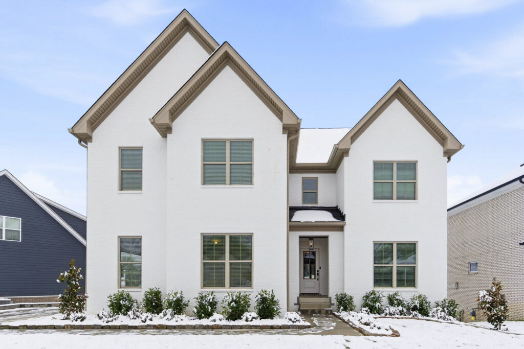 Front view of a white brick house with two steep gabled roofs, snow on the ground and a clear blue sky above