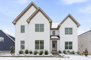 Front view of a white brick house with two steep gabled roofs, snow on the ground and a clear blue sky above