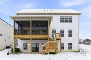 White two-story house with a large wooden deck and staircase in a snowy backyard.