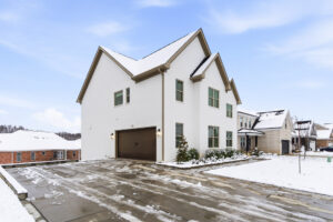 White two-story house with a brown garage door in a snowy suburban street.