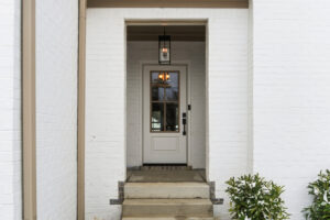 White brick entryway with a glass-paneled door and a hanging lantern above the doorway.