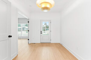 Bright entryway with white walls and a glass-pane door; natural light from outside and a warm ceiling light fixture above.